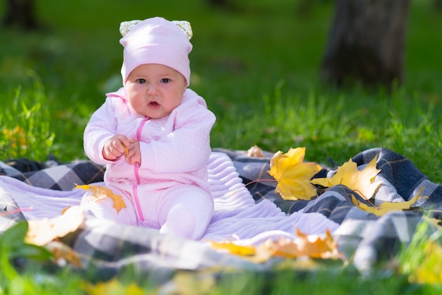 Un bebé con ropa rosa jugando sobre una alfombra de picnic entre hojas de otoño en una escena del parque.