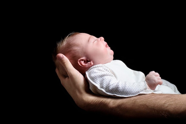 Foto bebé rubio dormido yace en la mano de un hombre fondo negro