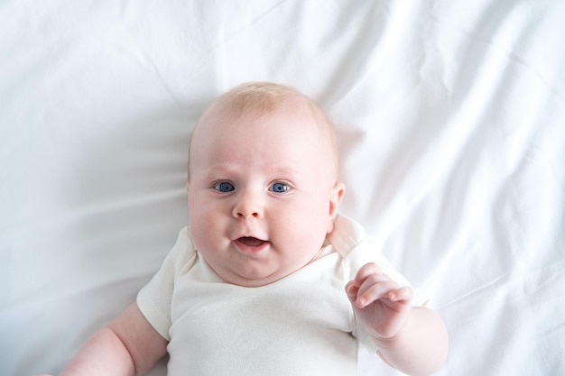 El bebé sano se acuesta boca arriba en la cama en la vista superior de la ropa de cama blanca