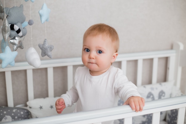 bebé sano en ropa blanca está sentado en la cama de un niño