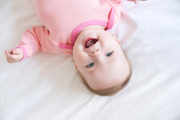 Un bebé sano y sonriente se acuesta boca arriba en la cama en la vista superior de la ropa de cama blanca