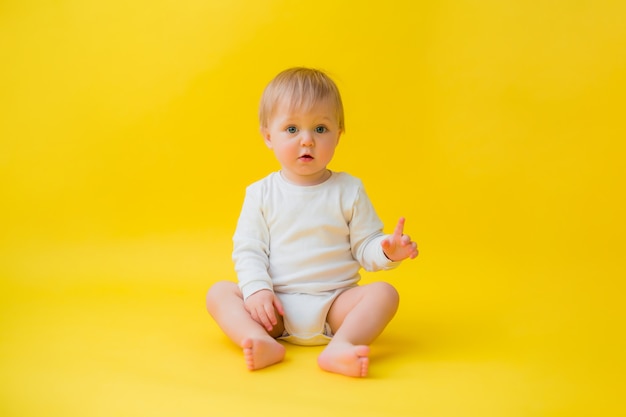 Bebê saudável em Body branco senta-se sobre um fundo amarelo, espaço para texto