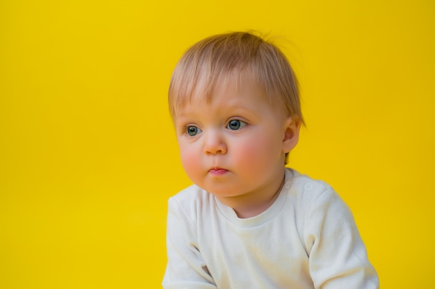 Bebê saudável em Body branco senta-se sobre um fundo amarelo, espaço para texto