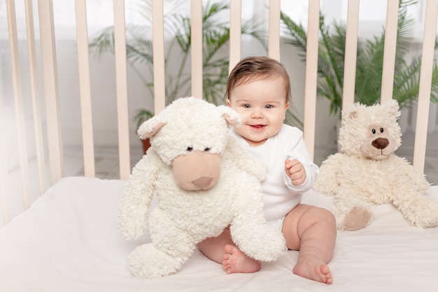 Bebé de seis meses jugando en una cuna con un mono blanco con un osito de peluche