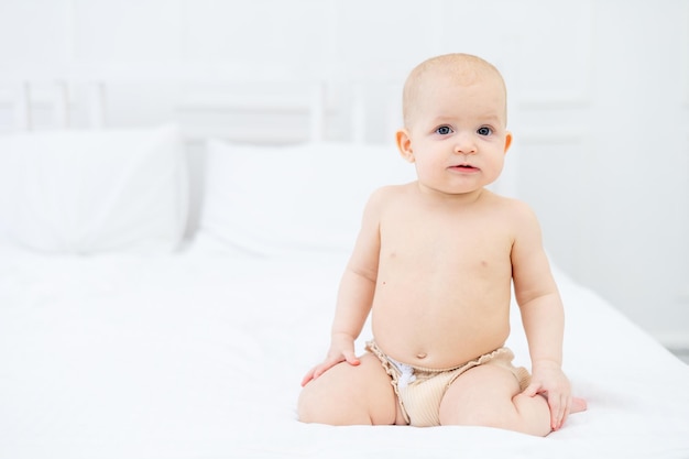 Un bebé de seis meses en pañales en una cama de algodón blanco en casa jugando y sonriendo