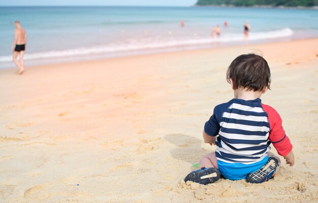 Foto bebê sente-se na praia jogando areia