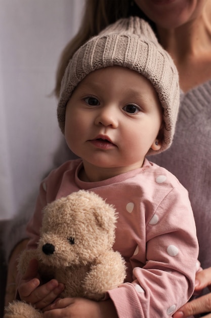 Foto un bebé serio en pijama rosa con lunares blancos se sienta en el regazo de su madre y sostiene un juguete en sus manos.