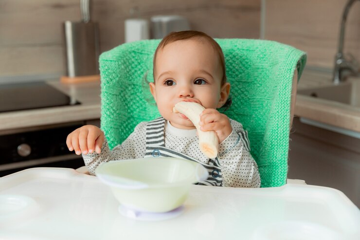 Foto el bebé se sienta en una silla alta en la cocina y come un plátano.