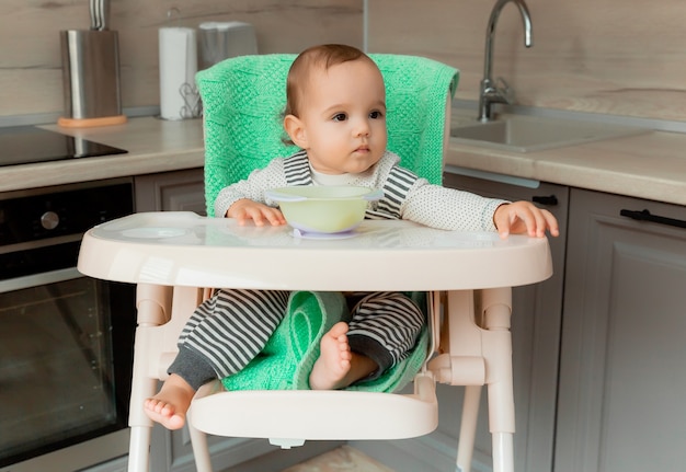 El bebé se sienta en una silla alta en la cocina y come un plátano.