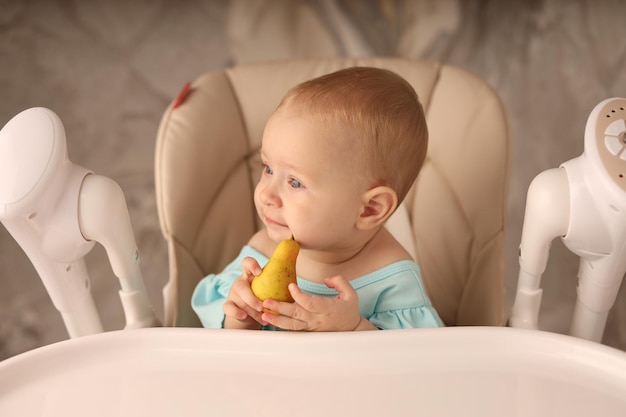 un bebé en una silla de alimentación come una pera solo