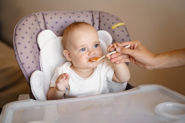 un bebé en la silla de un niño come puré de patatas con una cuchara