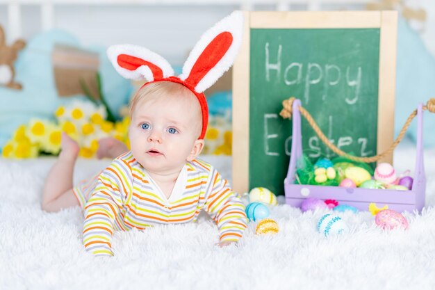 Foto un bebé con un sombrero de conejo en una cama con huevos de pascua y la inscripción feliz pascua