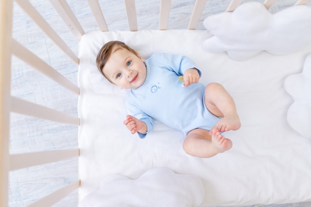 Bebé sonriente feliz en la cuna en traje azul, lindo bebé alegre en el dormitorio