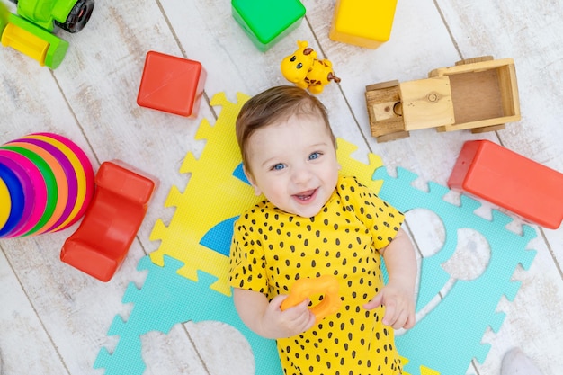 Un bebé sonriente y feliz juega en la guardería con un traje amarillo con juguetes de colores brillantes