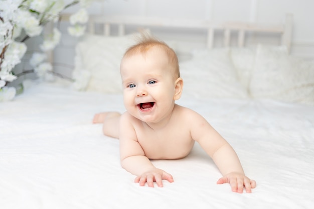 Bebé sonriente feliz en pañales en una cama de algodón blanco en casa de seis meses de edad.