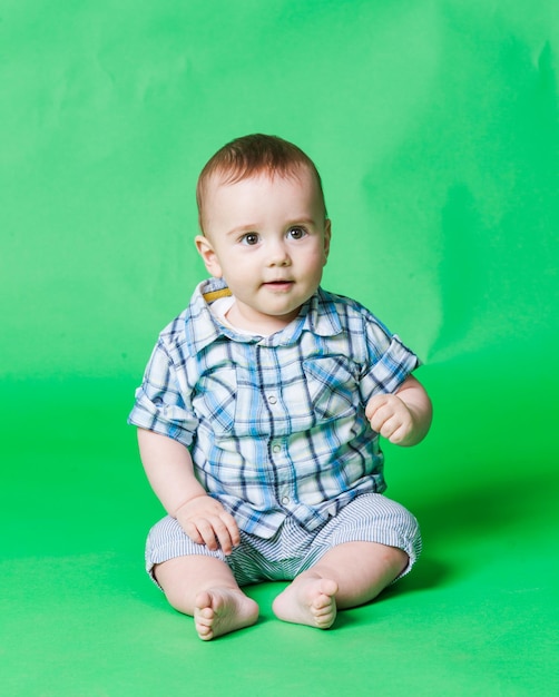 Bebé sonriente feliz sentado en el suelo mirando recto, fondo verde