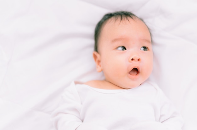 Bebé sonriente que miente en una cama blanca, mañana familiar en casa, higiene de niños.