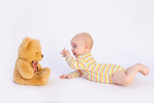 Bebé sonriente de seis meses se encuentra aislado con un suave oso de peluche