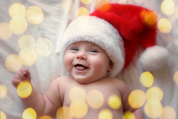 Bebé sonriente con sombrero rojo de Papá Noel celebrando la Navidad Lindo bebé recién nacido con sombrero de Navidad acostado en una manta blanca Feliz Navidad Feliz año nuevo Concepto de vacaciones para bebés Niño pequeño divertido
