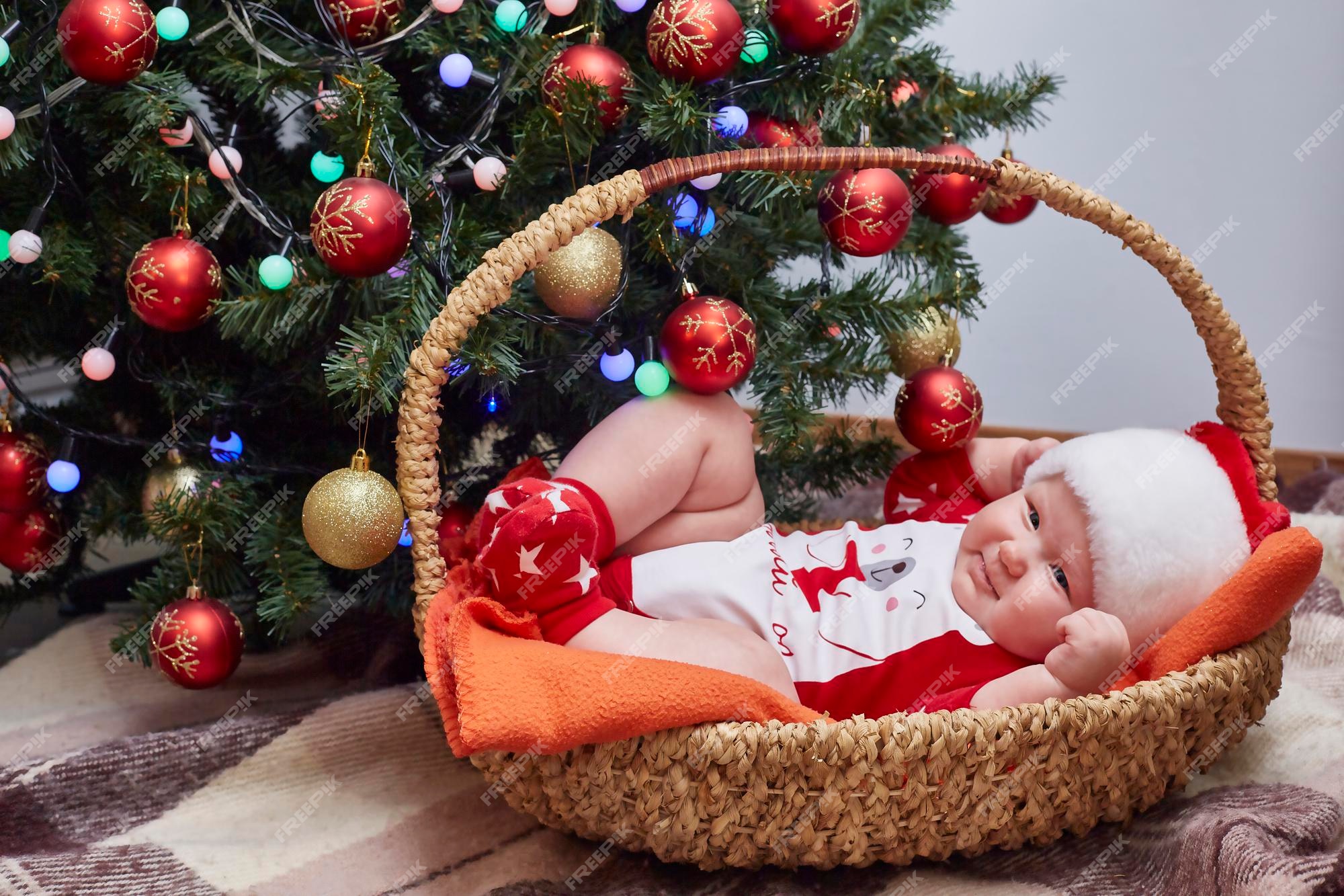 Bebé sonriente vestido con ropa de santa claus está acostado en una canasta del árbol de en casa. estilo de vida. el espacio. | Foto Premium