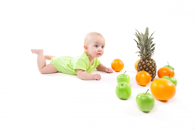 Bebê sorridente fofo deitado de bruços entre frutas e olhando