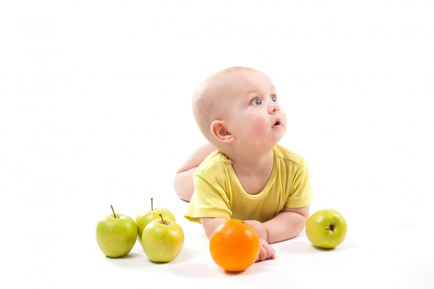 Bebê sorridente fofo deitado de bruços entre frutas e procurando