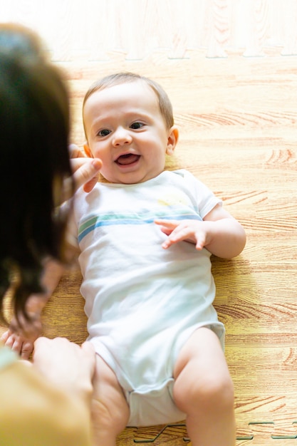 Foto bebê sorridente, olhando para sua mãe deitada no chão.