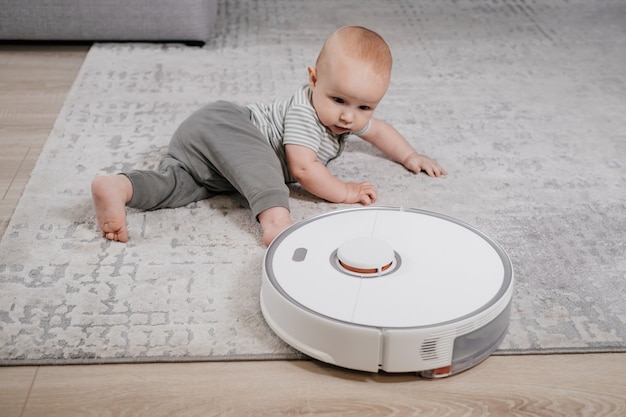 Bebé en el suelo con robot aspirador. Electrodomésticos para familias con hijos que facilitan la vida a la madre. Alfombra, alfombra de limpieza autónoma, dispositivo moderno para casa con niños.