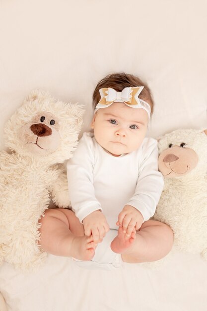 El bebé tiene seis meses en una cuna con un mono blanco con un osito de peluche.