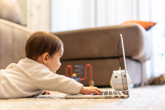 Bebé tirado en el suelo jugando con una computadora portátil