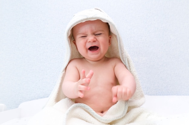 Bebé con una toalla en la cabeza se sienta y llora. Al niño no le gusta nadar.