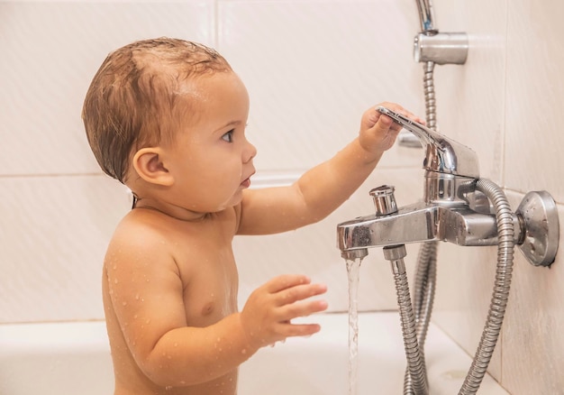 Bebê toma banho no banheiro segurando na torneira