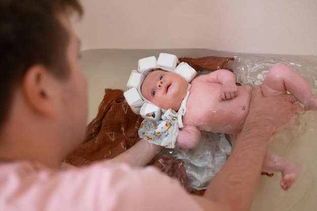 Bebê tomando banho com chapéu de natação especial. Pai segurando-a por segurança