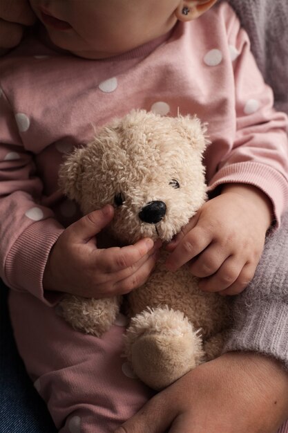 Un bebé con un traje rosa con lunares blancos sostiene un osito de peluche en sus manos.