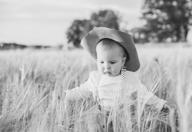 bebé en un traje con tirantes de pie en un campo con trigo