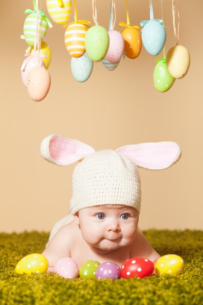 Bebé de tres meses acostado boca abajo como un conejito de Pascua en la hierba con huevos