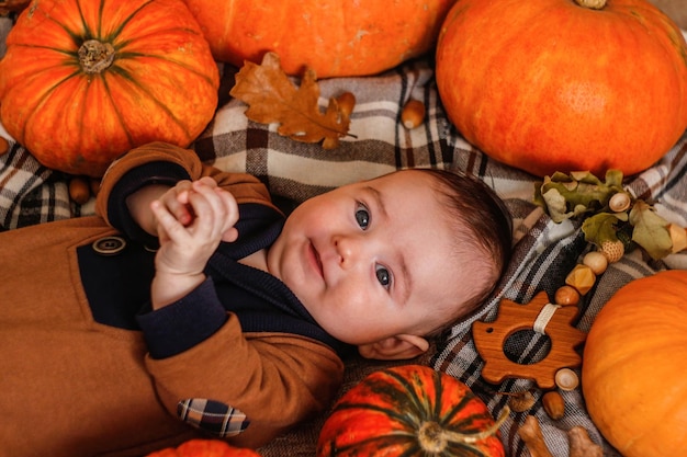 Un bebé de tres meses yace con calabazas en una manta Chico lindo posando en el fondo de una calabaza