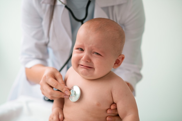 Bebê triste sendo examinado por um médico com um estetoscópio