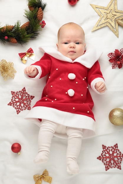 Bebé vestido para la primera Navidad con decoración navideña sobre fondo blanco. Foto vertical