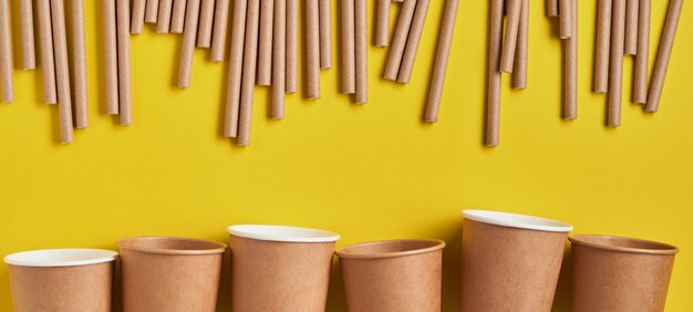 Bebederos hechos de papel y maicena, material biodegradable y vasos de papel ecológico sobre fondo de color amarillo tendencia 2021. Concepto libre de desperdicio cero y plástico. Bandera. Vista superior.