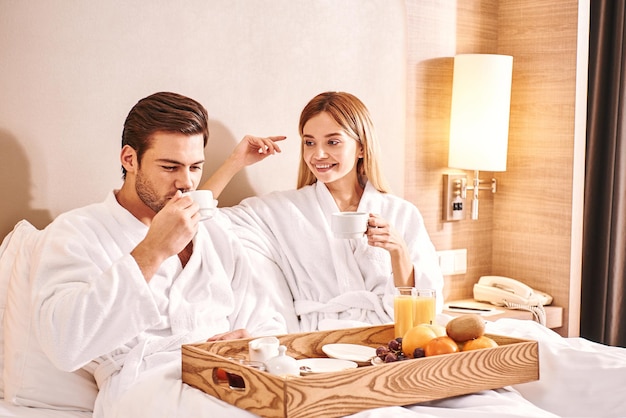 Bebendo café da manhã no quarto de hotel, casal está comendo na cama do quarto de hotel