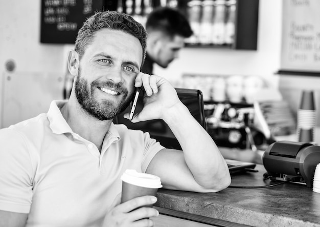 Beber café mientras espera Esperando por usted Hombre teléfono inteligente pedir café en la cafetería Concepto de pausa para el café Opción de llevar café para personas ocupadas Hombre conversación móvil café barista fondo