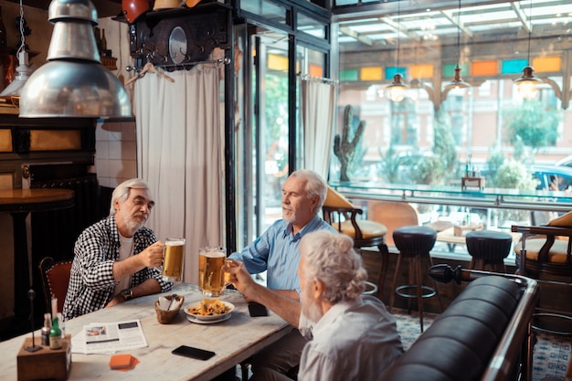 Beber cerveza juntos. Tres hombres que se sienten bien mientras beben cerveza juntos en el pub