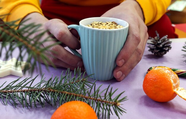 Beber chá aconchegante nos dias de inverno. Uma xícara de chá nas mãos, tangerinas, ramos de abeto, doces, cones, vista lateral