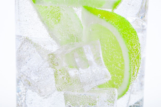 Beber del hielo, trozos de lima verde jugosa fresca y agua cristalina en un vaso.