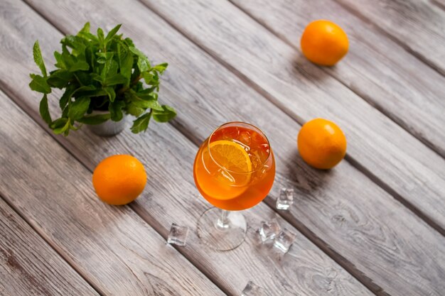 Beber con rodaja de naranja. Naranjas sobre superficie de madera. Aperol rociado con vino espumoso. Menta fragante en balde pequeño.