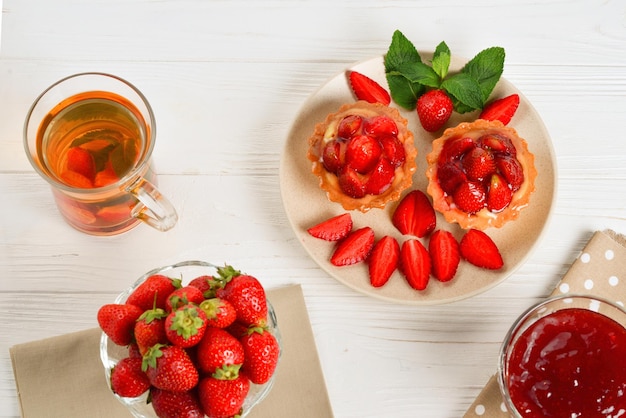 Beber té con tartaletas y pasteles con fresas