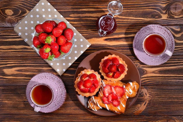 Beber té con tartaletas y tortas con fresas