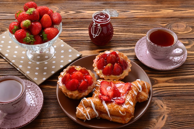 Beber té con tartaletas y tortas con fresas