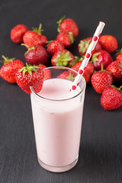 Beber yogur de fresa en el vaso con una pajita sobre una pizarra negra